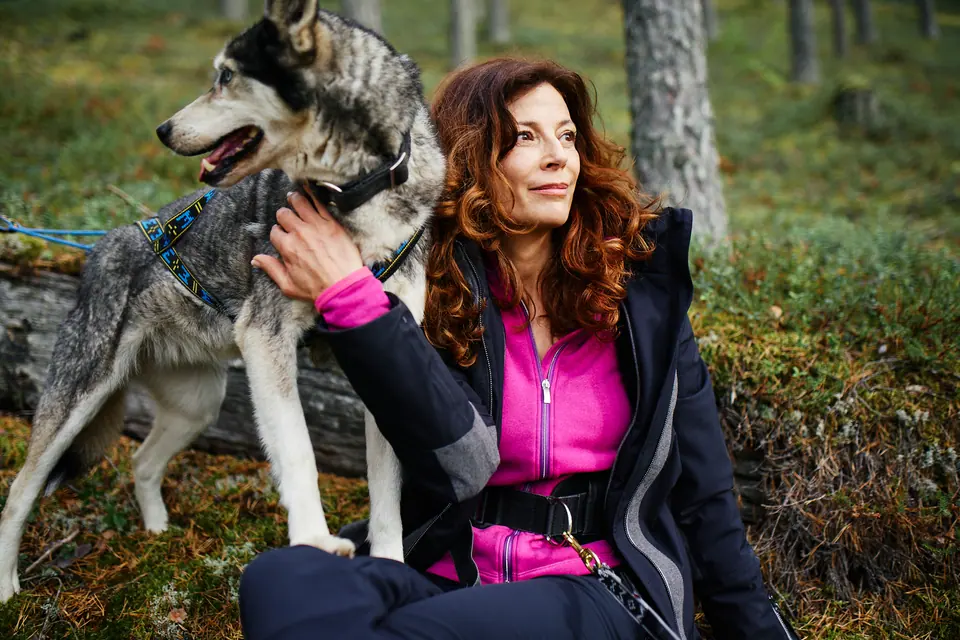 Person mit Outdoorjacke und Hund im Wald