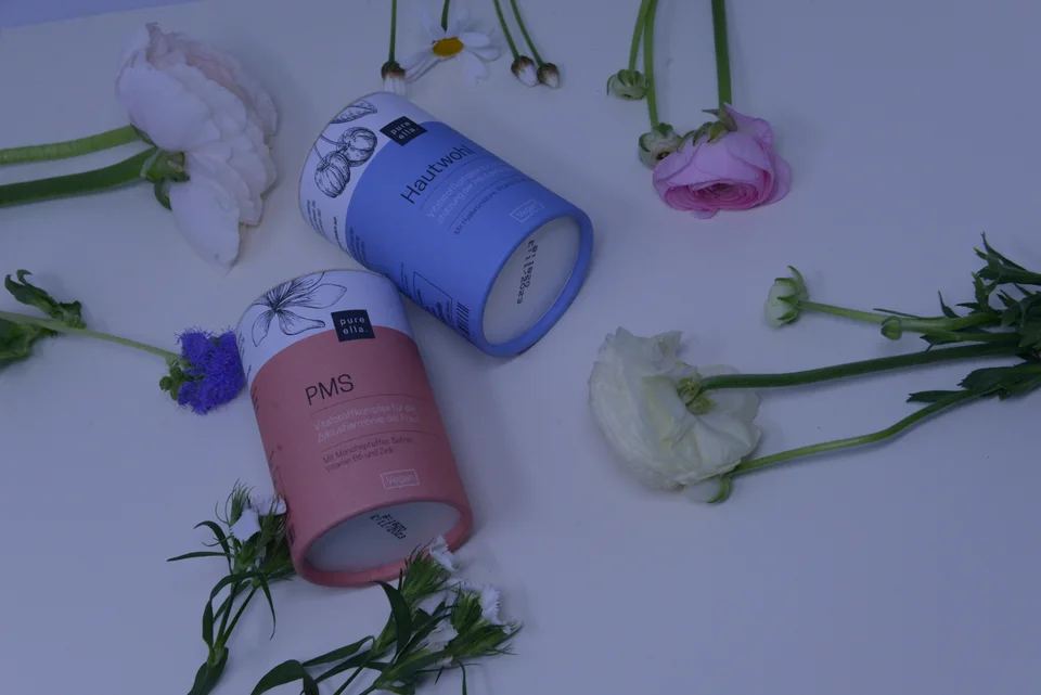 Pure-Ella-Produktpackungen mit Blumen in einer fotografischen Draufsicht