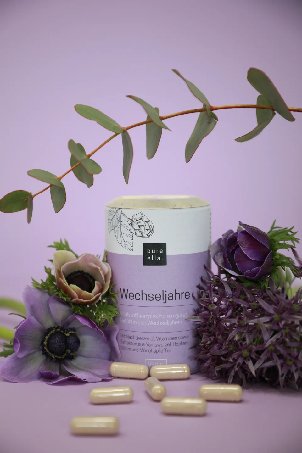 Pure-Ella-Produkt mit Zweigen und Blüten vor lilafarbenem Hintergrund