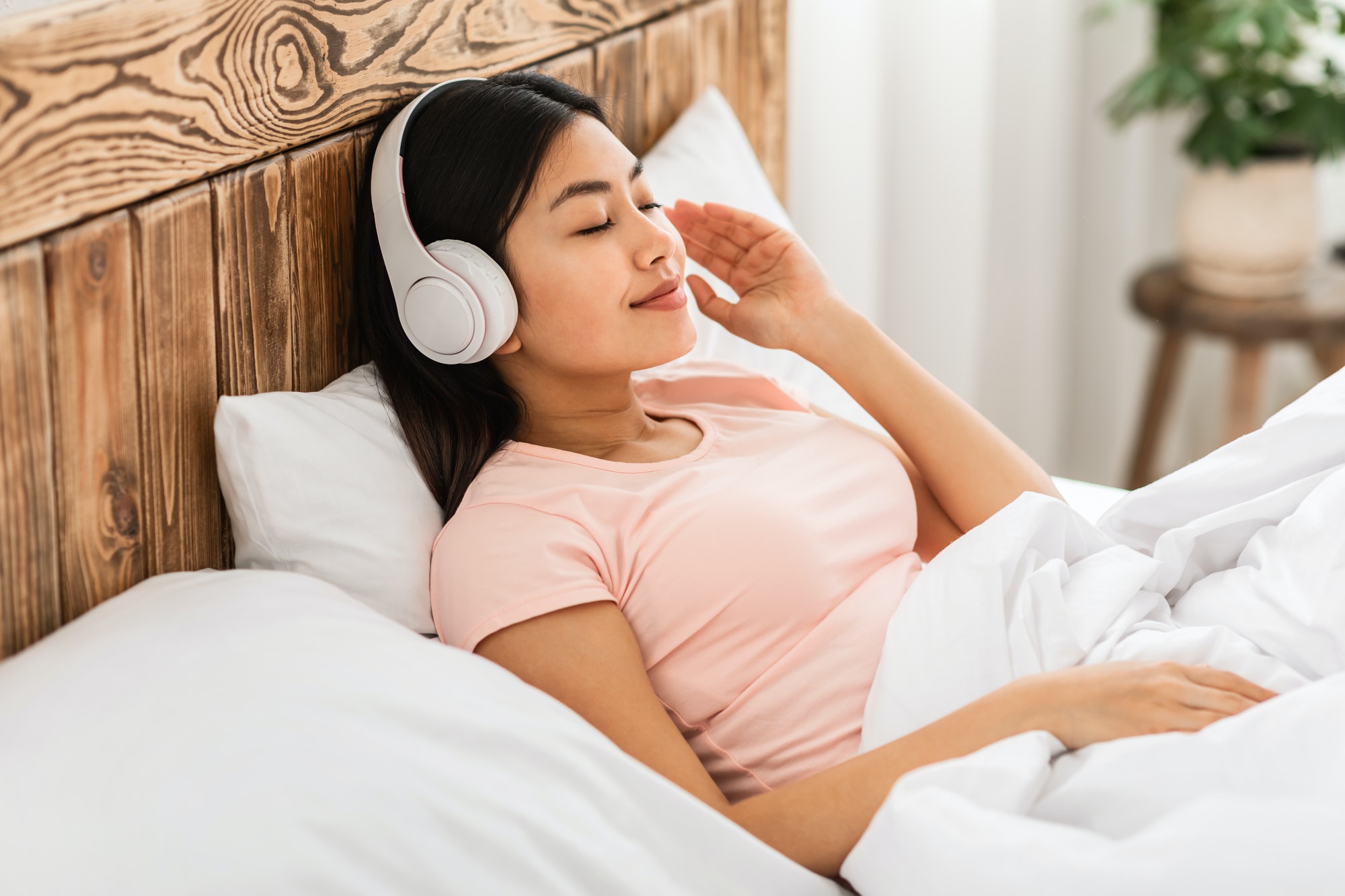 Chinese Girl In Earphones Listening To Podcast Lying In Bed